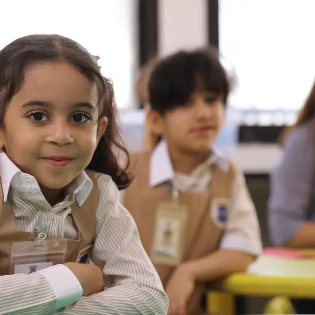 A pigtailed AFS pupil smiling with arms crossed at her classroom desk