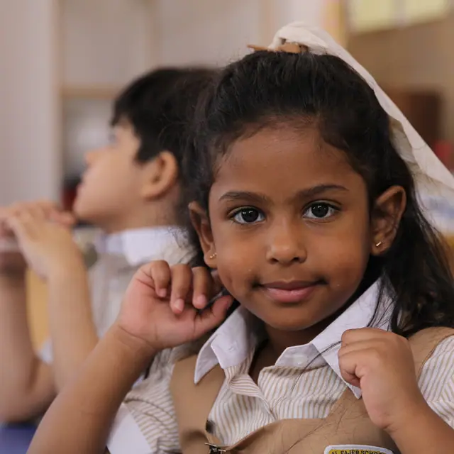 A pupil with a white hair bow smiling in a warm classroom