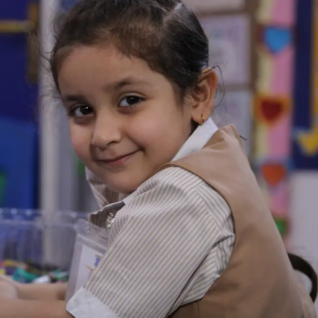 A smiling kindergarten pupil turning from her craft table with crayons