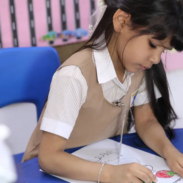A focused girl colouring at a blue classroom table