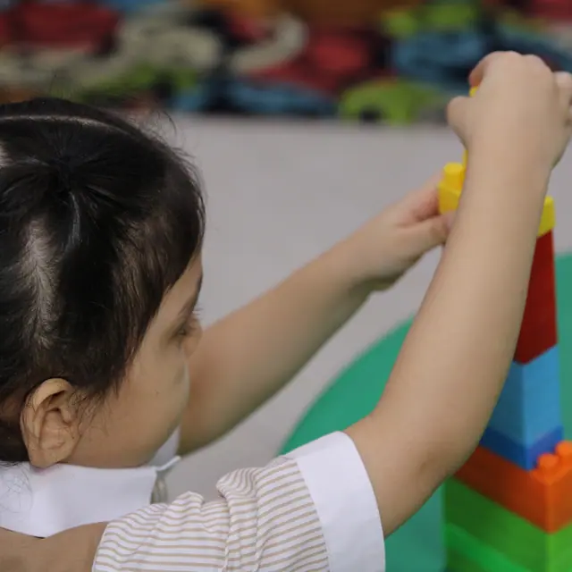 A girl with a gold hair bow stacking colourful blocks