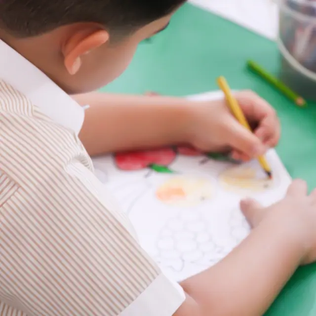 An over-shoulder view of a pupil colouring a fruit worksheet