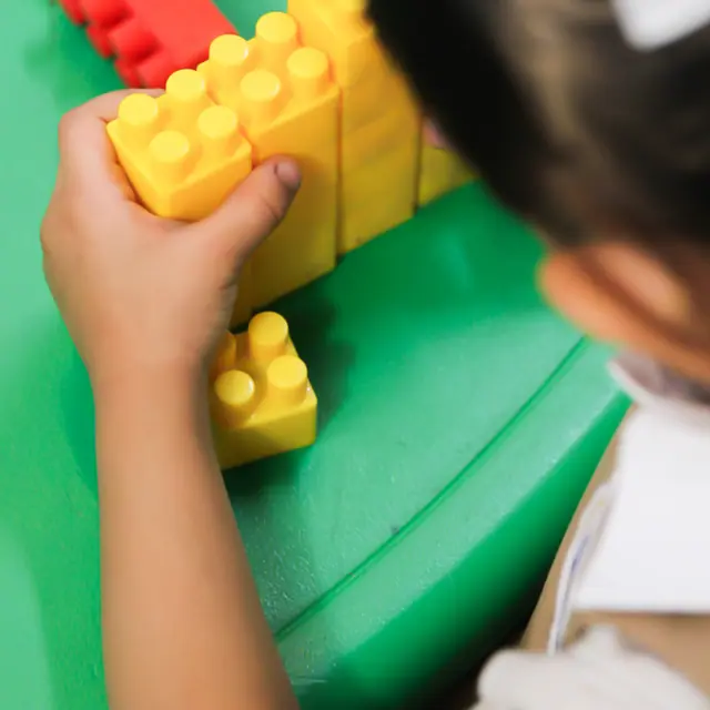 A child's hands building with yellow toy blocks