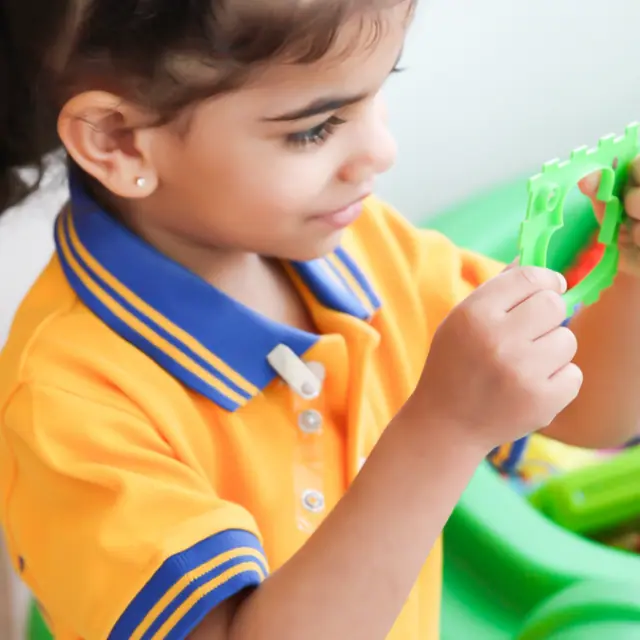 A girl in a gold-and-blue polo playing with a toy at an activity table