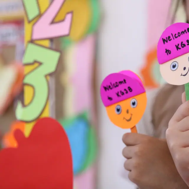 A child holding up two smiley-face welcome stick puppets