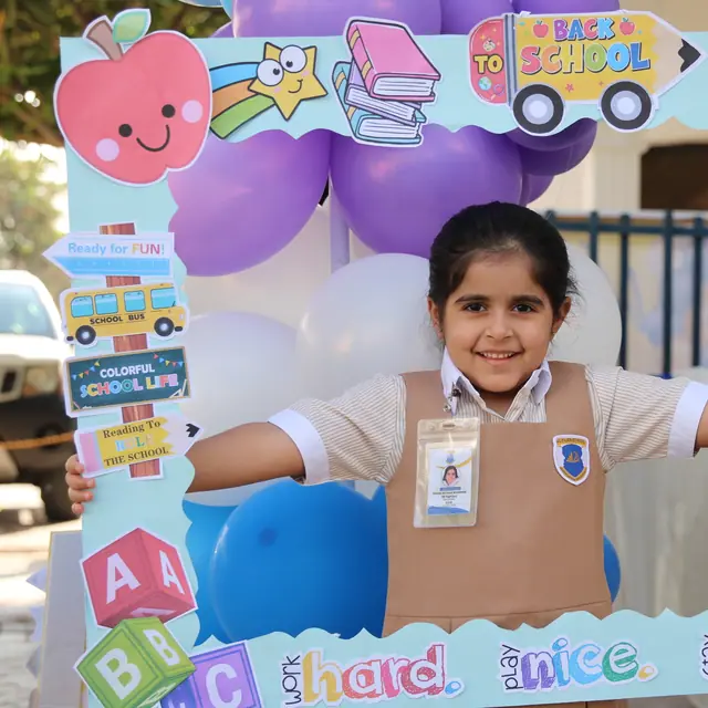 A girl smiling in the Back to School selfie frame with balloons behind