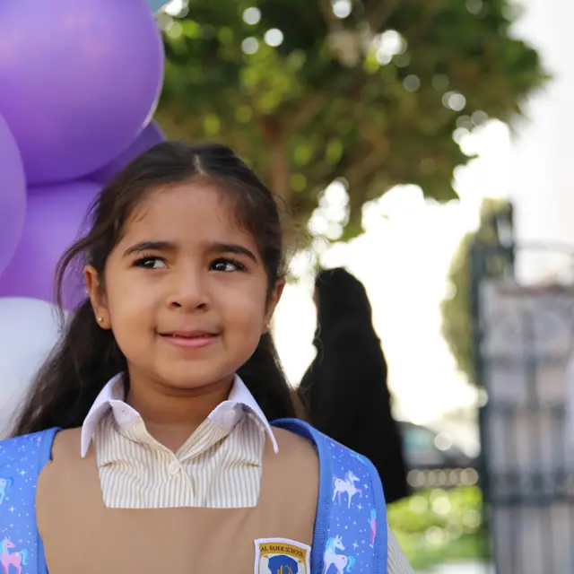 A girl with a unicorn backpack glancing sideways with a shy smile