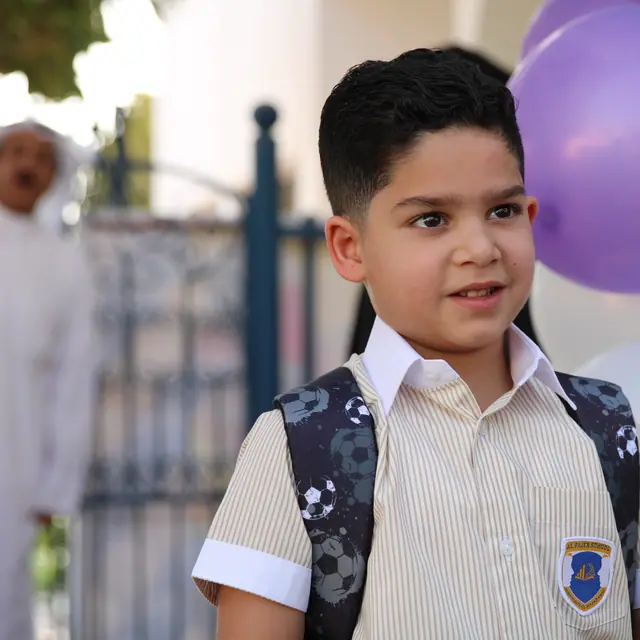 A boy with a backpack smiling in front of the balloon arch at the school gate