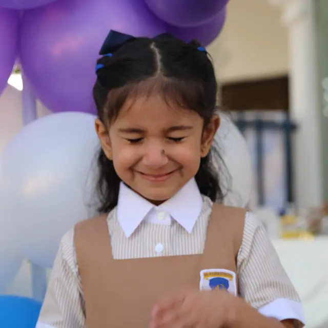 A girl giggling with eyes closed in front of purple and white balloons