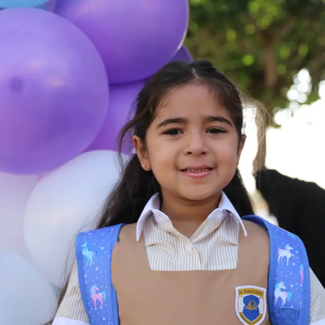 A smiling girl with unicorn backpack straps in front of pastel balloons
