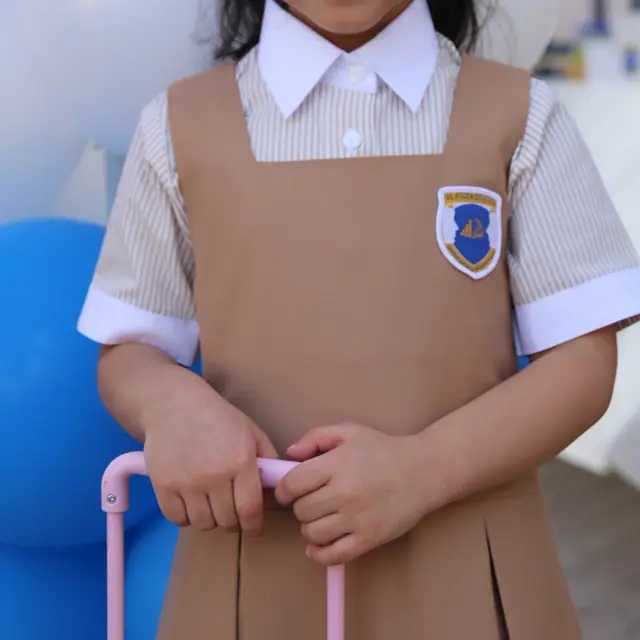 A beaming girl with hair bows holding her pink suitcase in front of a balloon arch