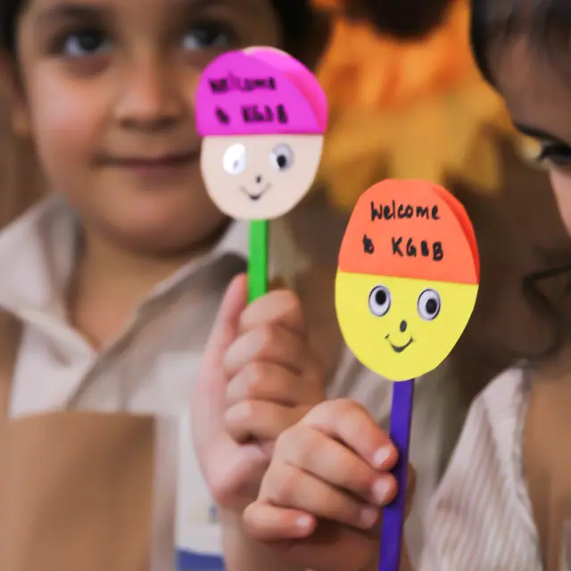 Two KG children holding up handmade welcome stick puppets