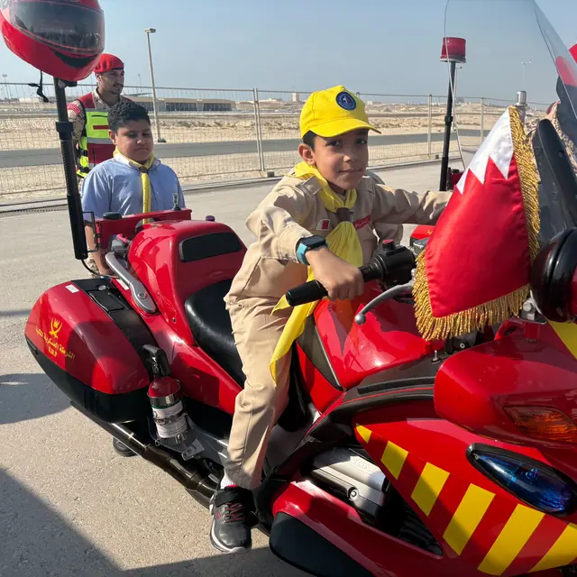 A boy in a yellow scout cap at the handlebars of a police motorcycle