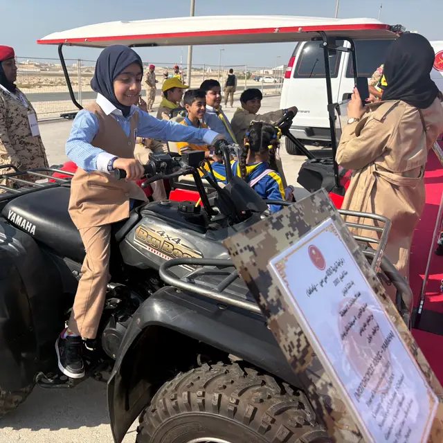 A pupil in hijab climbing onto an ATV with classmates behind