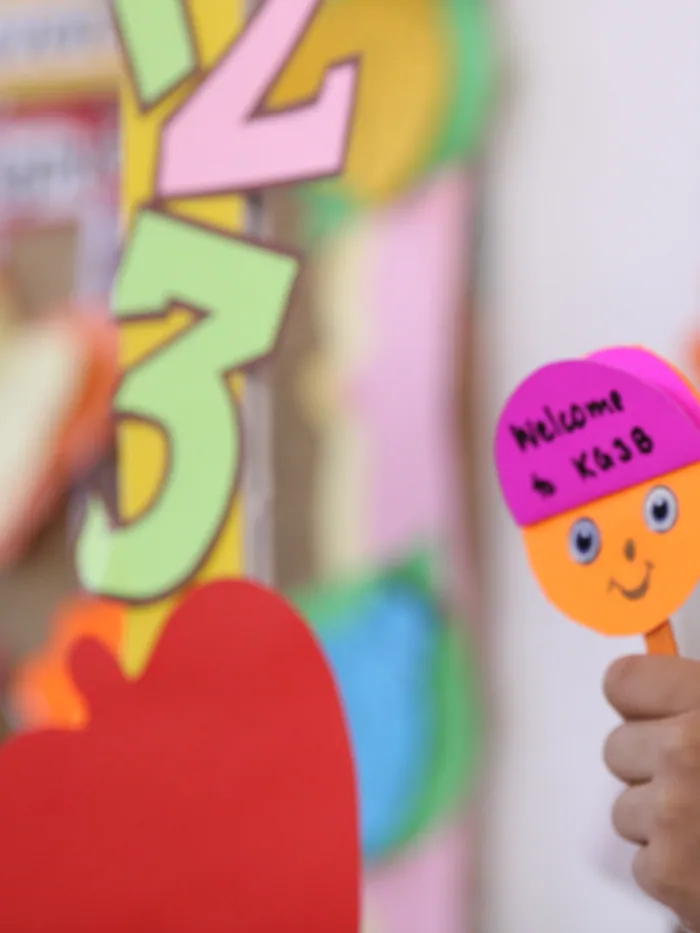 A child holding up two smiley-face welcome puppets made in class