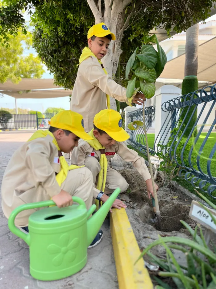 AFS scouts in yellow caps planting a sapling by the school fence