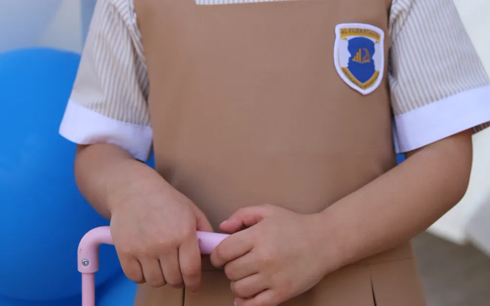 A young AFS pupil in her school pinafore holding the handle of a pink suitcase